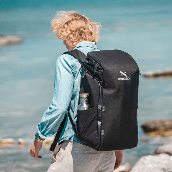 Man går vid havet med en svart praktisk ryggsäck på 30 liter som har en termos i sidofacket